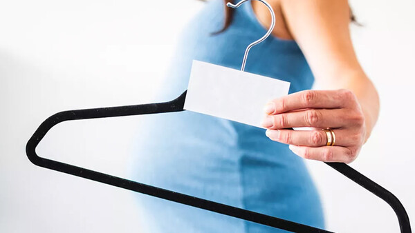 Person holding a clothing hanger with a blank white price tag or label attached.