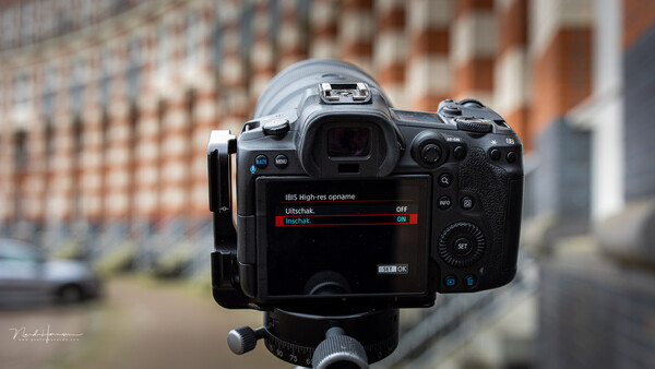 Mirrorless camera mounted on tripod displaying menu settings with urban brick building backdrop.