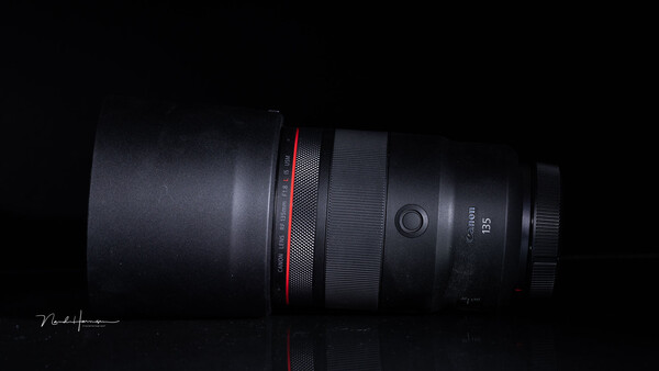 Canon RF 135mm telephoto lens positioned horizontally against black background with red accent band visible.