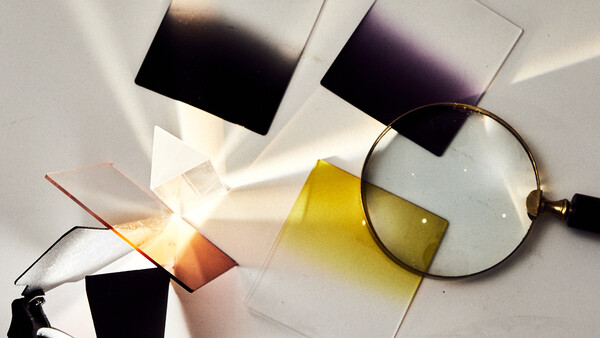 Color filter swatches and a magnifying glass arranged on white paper with warm sunlight casting shadows.