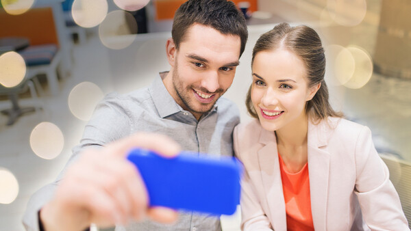 Two smiling business professionals taking a selfie with a blue smartphone.