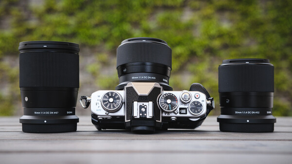 Vintage rangefinder camera with three interchangeable lenses arranged symmetrically on wooden surface.