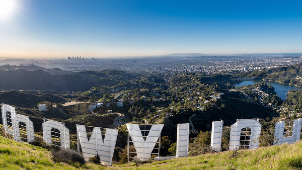 Large white letters spelling "HOLLYWOOD" on a hillside overlooking a sprawling cityscape with mountains in the distance.