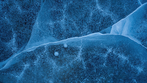 Aerial view of a frozen lake with thin cracks in the ice and scattered snow across the surface.