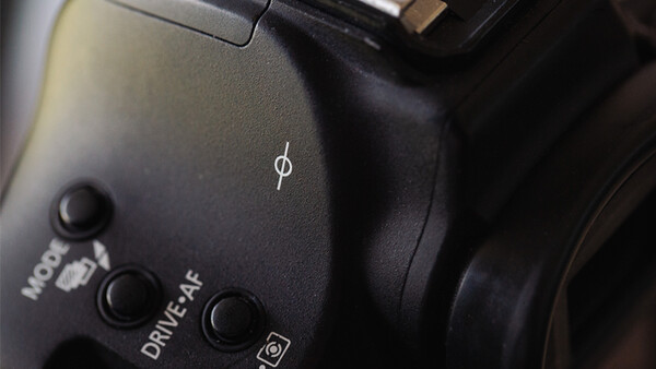 Close-up of camera body controls showing mode dial, drive settings, and ISO button with dramatic side lighting.