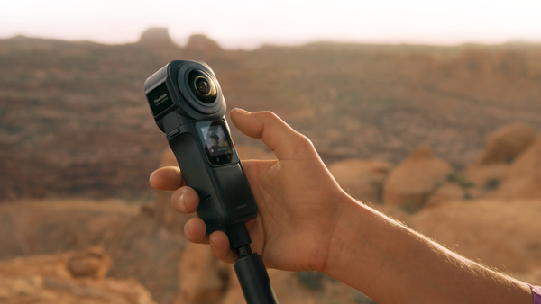Hand holding a compact 360-degree action camera against a desert landscape backdrop.