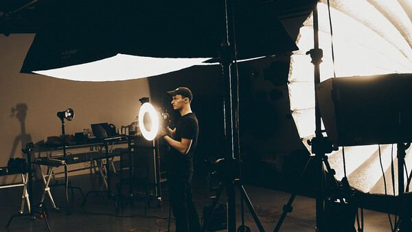 Photographer adjusting a large circular ring light on a studio set with multiple lighting rigs and diffusion panels.