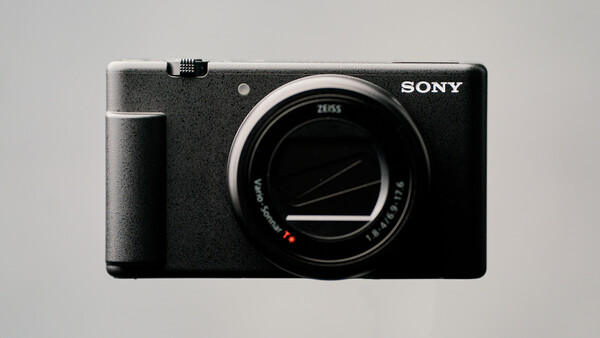 Sony mirrorless camera body with Zeiss lens shown against neutral gray background.