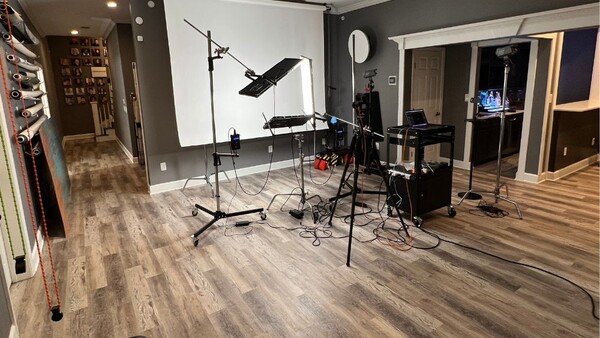 Professional home studio setup with drum kit, microphones, lighting rigs, and acoustic treatment on gray walls.