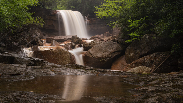 Waterfall cascading over rocky ledge surrounded by dense green forest foliage.