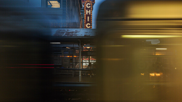 Motion-blurred subway train passing in front of historic theater marquee at dusk.
