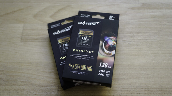 Three black boxes of Exascend Catalyst CompactFlash memory cards with 128GB capacity displayed on a wooden surface.