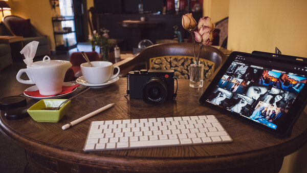 Photographer's desk setup with camera, keyboard, tablet displaying images, and coffee cups on wooden round table.