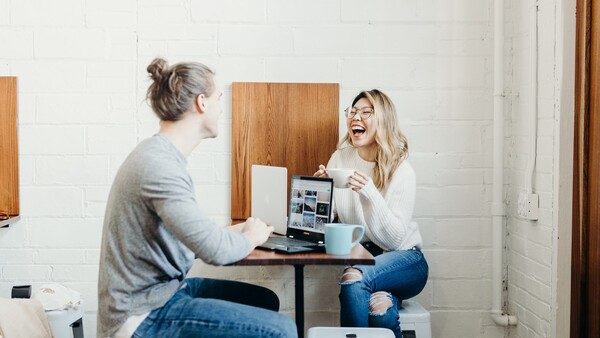 Two women sitting at a small table having a conversation and laughing in a bright studio space.