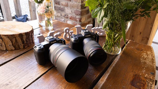 Two mirrorless cameras with telephoto lenses displayed on a wooden table in a studio setting.