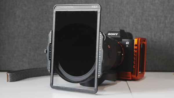 Smartphone mounted in a rig holder with a Sony mirrorless camera and red LED light panel on a white surface.