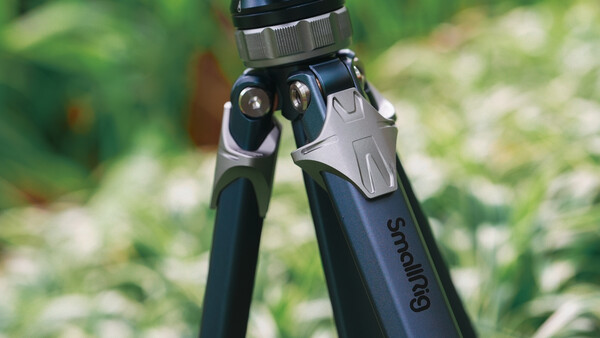 Close-up of a tripod head with ball joint and adjustment knobs against a blurred green outdoor background.