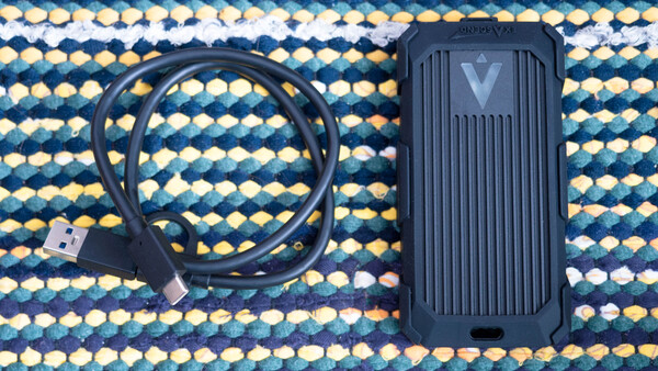 External SSD with USB cable on a patterned textile background.