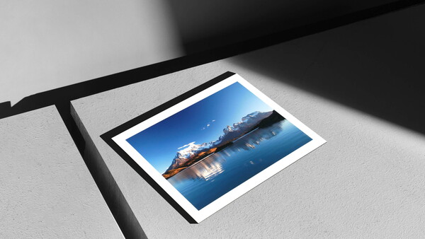 Polaroid-style photograph of a cargo ship on calm blue ocean water displayed on white surface with dramatic shadow.