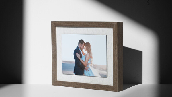 Framed photograph of a couple embracing outdoors displayed in a rustic wood frame with white mat.