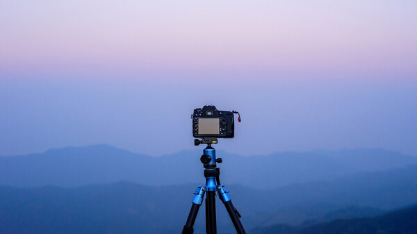 DSLR camera mounted on blue tripod against layered mountain silhouettes at twilight.