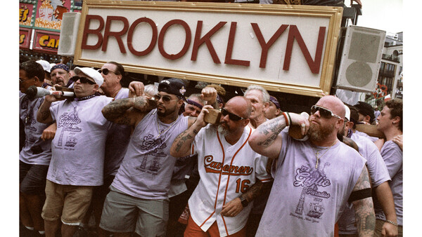 Group of people holding a large illuminated Brooklyn sign above their heads during a daytime outdoor gathering.