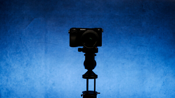Sony mirrorless camera mounted on a tripod against a deep blue textured background.