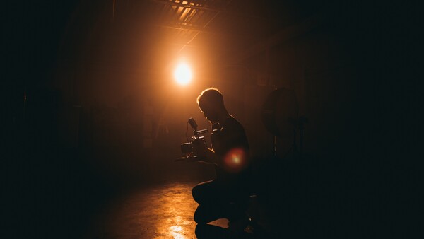 Silhouetted figure holding a camera in a dark corridor, backlit by warm golden light.