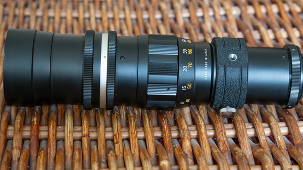 Vintage telephoto lens disassembled showing internal glass elements and mechanical components on woven surface.