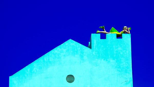 Minimalist architectural photograph of a bright cyan building with geometric forms against a deep blue sky.