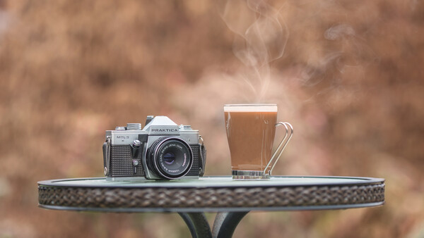 Vintage rangefinder camera and glass of beer on decorative table with blurred brown background.