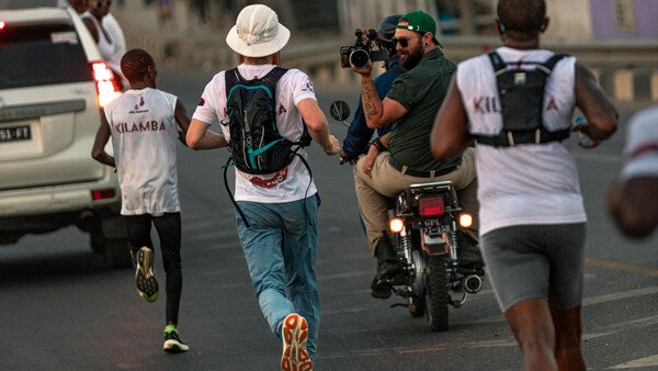 Urban street runners moving past a motorcyclist during daytime in a busy city setting.