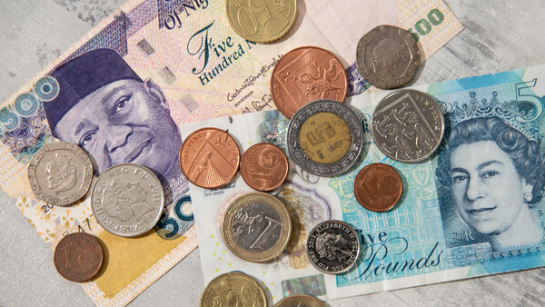 British banknotes and coins arranged on a white surface, including a £5 note and £10 note with various denominations of coins.