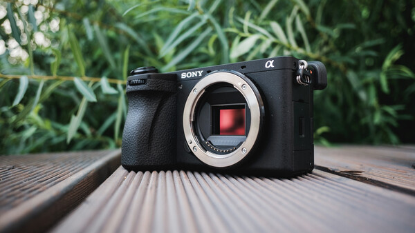 Sony Alpha mirrorless camera body displayed on wooden surface with blurred foliage background.
