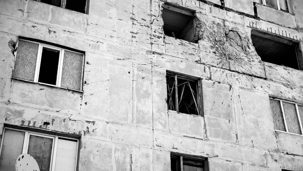 Abandoned concrete apartment building with boarded windows and crumbling facade.