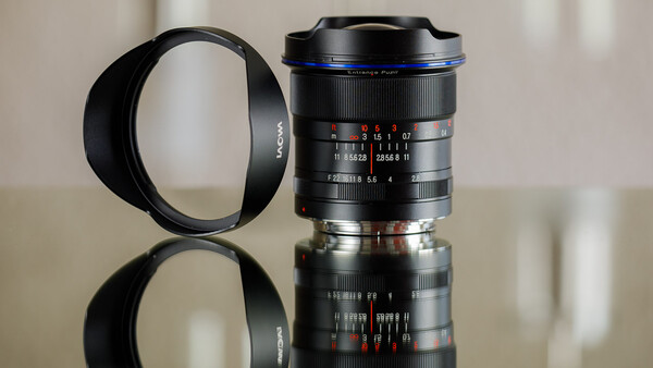 Two vintage manual focus lenses with lens hoods displayed against a neutral background with reflections.