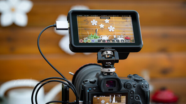 External monitor mounted on camera showing live video feed with editing interface and flower graphics.