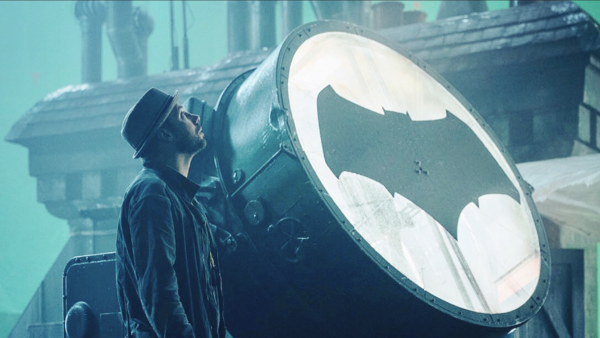 Photographer positioning a large reflective dish toward a subject in an urban setting with cyan-tinted lighting.