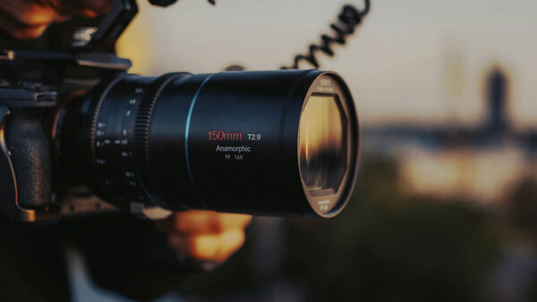 Close-up of a 150mm T2.9 anamorphic lens mounted on a camera, with a blurred cityscape in the background during golden hour.