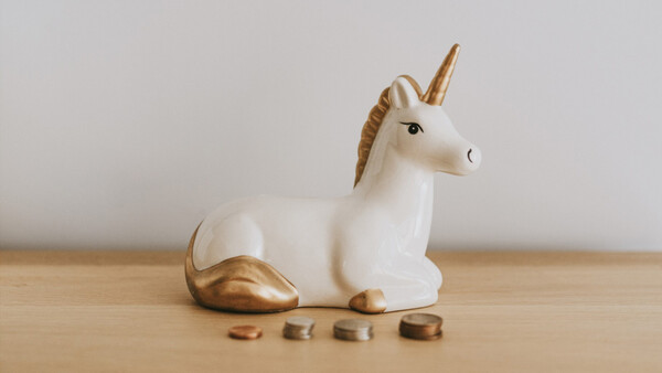 White ceramic unicorn figurine with gold accents and four small gold coins arranged in front.