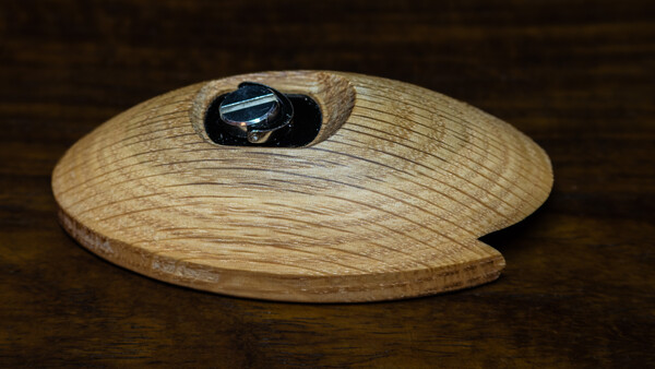 Wooden oval dish with grain texture and a dark metal ring recessed into its surface.