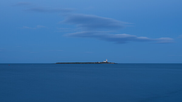 Cargo ship on the horizon under a blue sky with wispy clouds and calm sea.