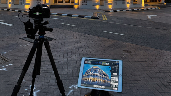 Professional camera on tripod pointed at tablet displaying architectural photograph on urban street at dusk.