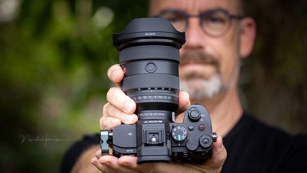 Photographer holding Sony mirrorless camera with telephoto lens, displayed toward camera.