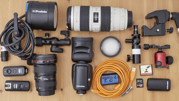 Professional photography equipment laid out flat on wooden surface including lighting, lenses, cables, and accessories.