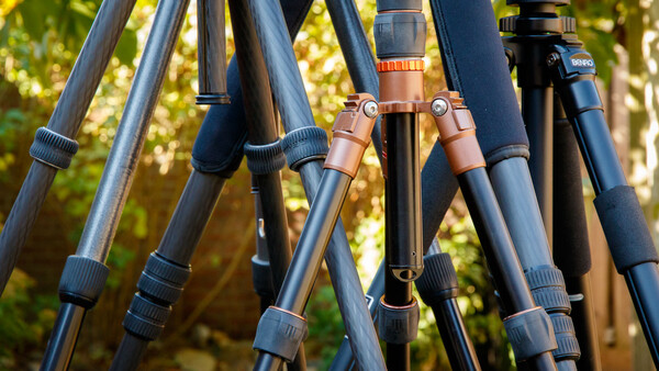 Close-up of multiple tripod legs with adjustment knobs and leather connectors against a blurred green forest background.