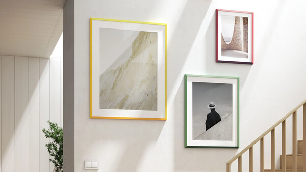 Three framed artworks displayed on a white wall beside a wooden staircase.