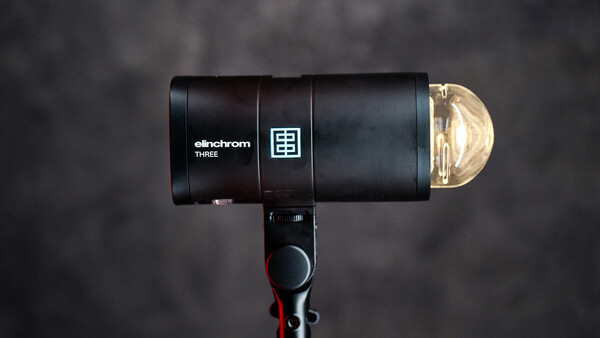 Elinchrom THREE monolight with reflector dome positioned against a dark textured backdrop.
