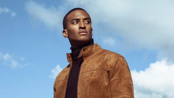 Man in tan suede jacket photographed against blue sky with clouds.