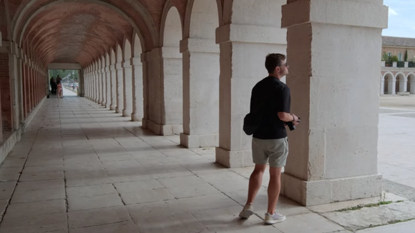 Runner jogging through a covered colonnade with repeating arches and columns.